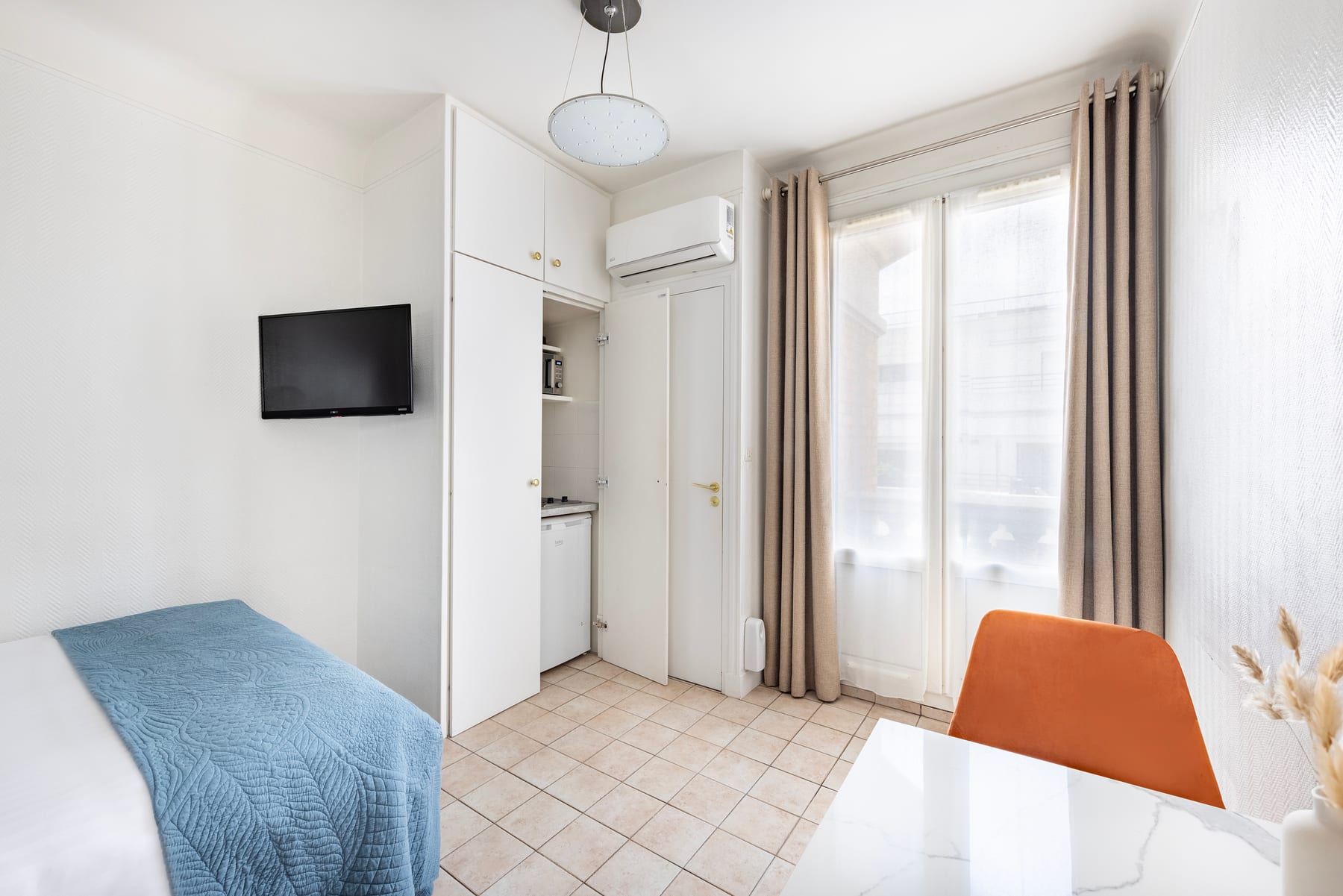 Studio Éco : espace nuit, kitchenette, télévision et coin repas près de la fenêtre